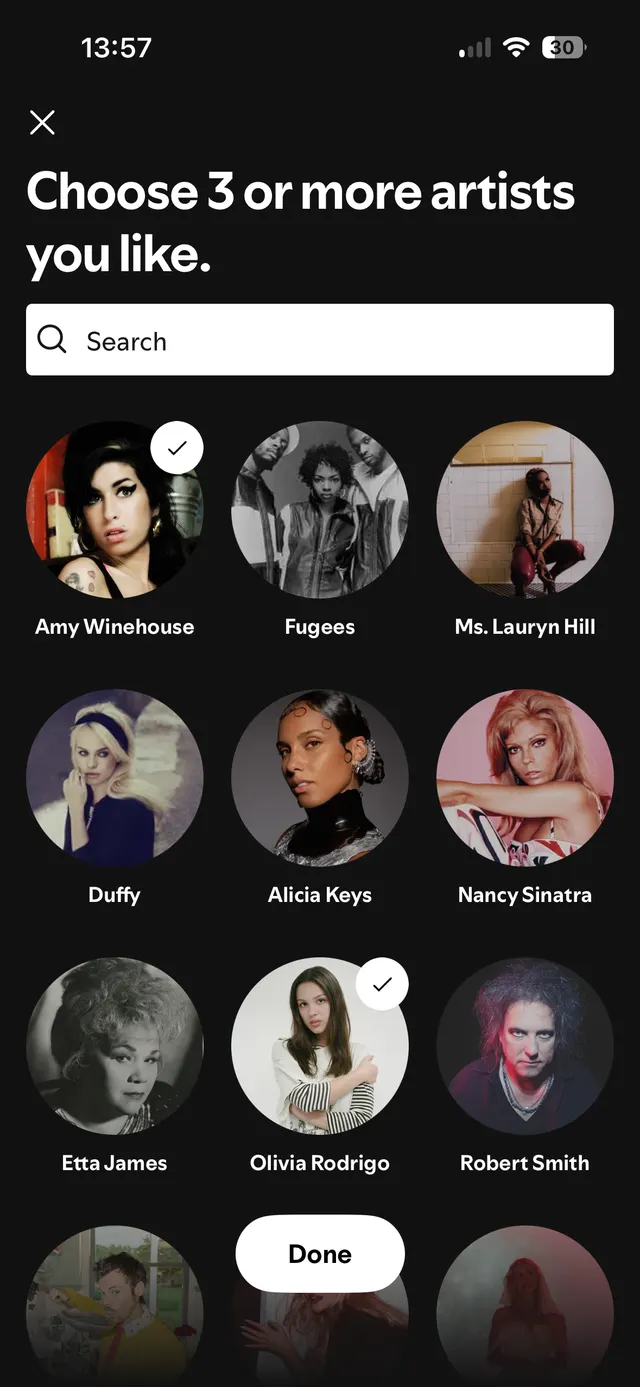 A selection screen titled 'Choose 3 or more artists you like.' There is a search bar followed by circular artist profile images with names underneath. Some artists are selected with a checkmark.
