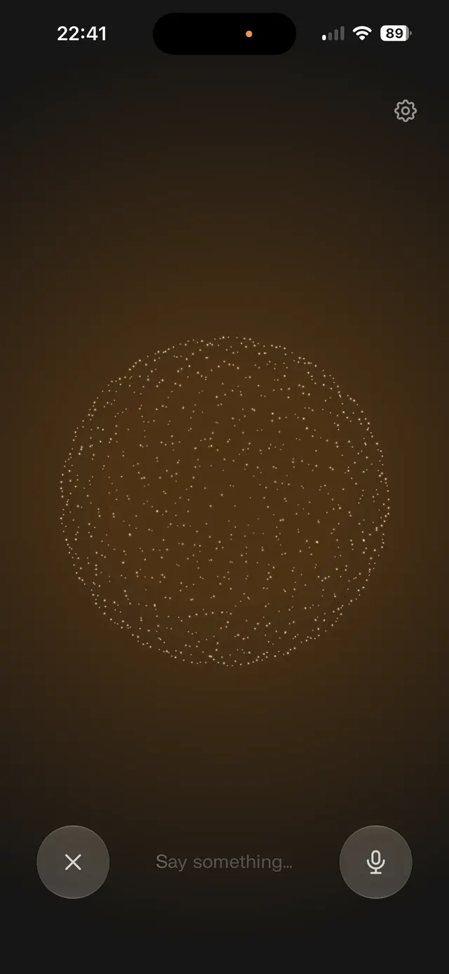 Dark voice assistant screen with a large animated dotted sphere in the center, a text prompt saying 'Say something...', a microphone button, a close button, and a settings icon.