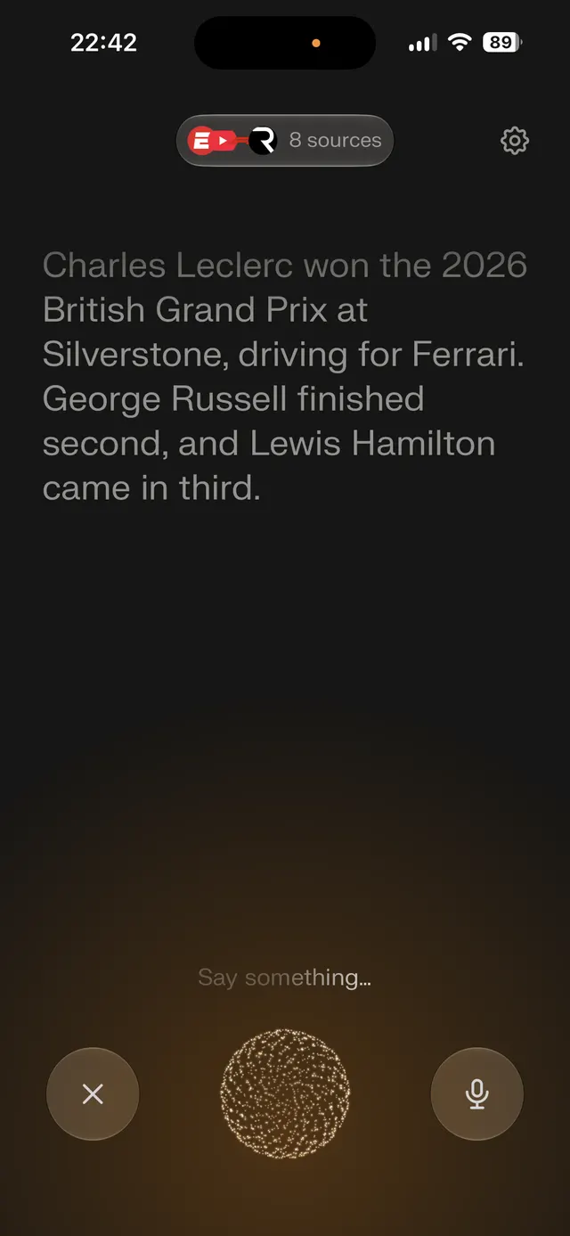 Dark mobile screen showing a spoken-answer interface with a large text response about the 2026 British Grand Prix, a sources pill near the top, a settings icon, and bottom controls for cancel and microphone with a pulsing orb in the center.